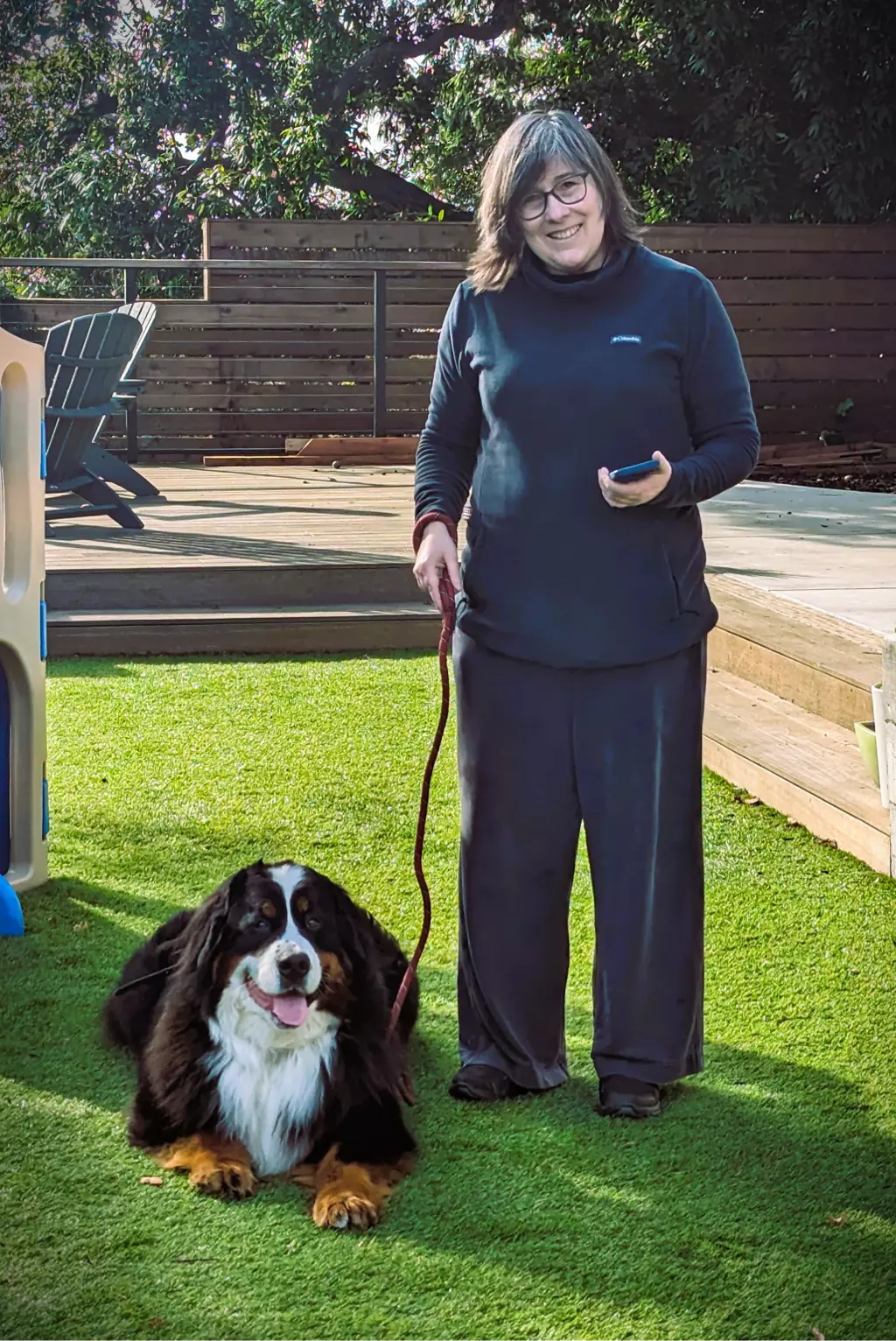 Woman with Bernese Mountain Dog on leash outdoors.